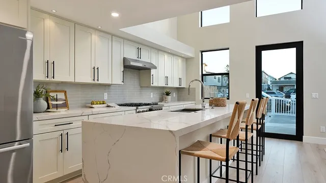 a kitchen with stainless steel appliances granite countertop a stove a refrigerator a sink a dining table and chairs with wooden floor