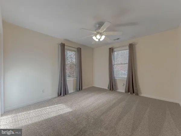 an empty room with a chandelier fan and windows