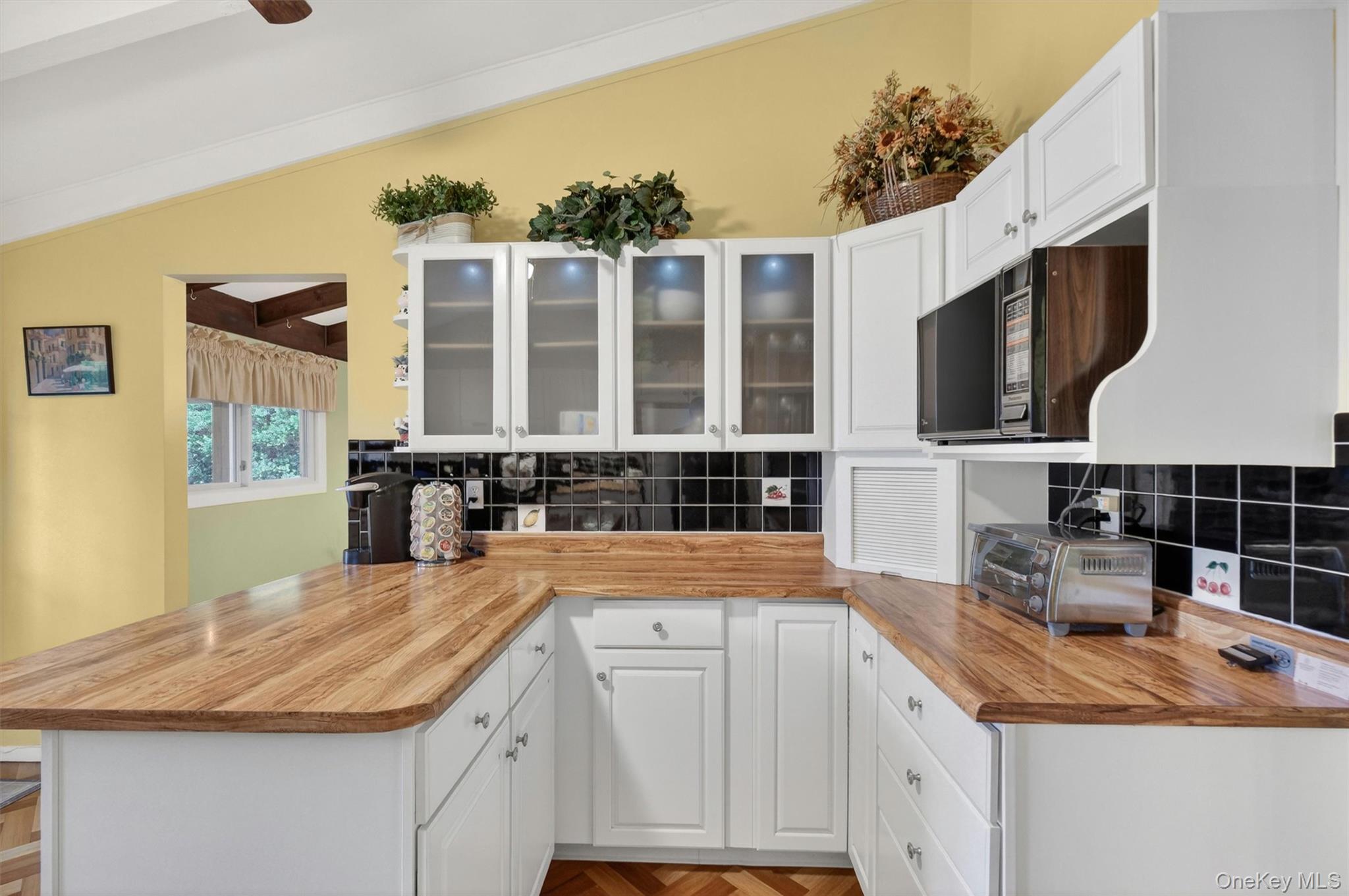 1 Rockledge Road Poughkeepsie, NY 12601 - Photo 12 of 36 Kitchen featuring vaulted ceilings with exposed beams, wood-finish flooring in a herringbone pattern, white cabinetry, breakfast bar, tile backsplash, cabinet lighting and light wood-finish countertops