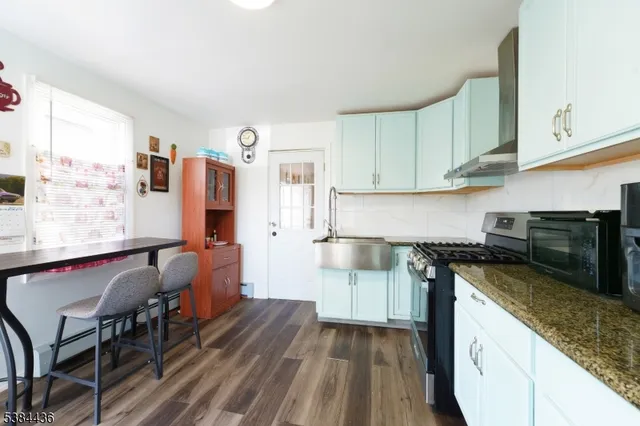 a kitchen with stainless steel appliances granite countertop a stove top oven a sink dishwasher and white cabinets with wooden floor