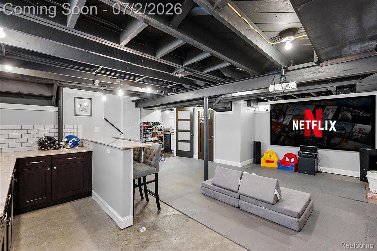 1706 Princeton Road Berkley, MI 48072 - Photo 41 of 49 Finished basement featuring a built-in wet bar with dark wood cabinetry and subway tile backsplash, a large projection screen, exposed ceiling beams, and concrete flooring
