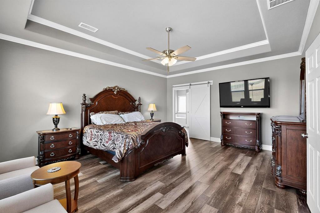 634 Gant Road Sherman, TX 75090 - Photo 19 of 40 Bedroom featuring a tray ceiling, a barn door, dark wood-style floors, ornamental molding, and ceiling fan