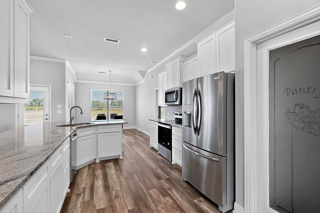 634 Gant Road Sherman, TX 75090 - Photo 7 of 40 Kitchen featuring ornamental molding, stainless steel appliances, white cabinets, light stone counters, and dark wood-style flooring