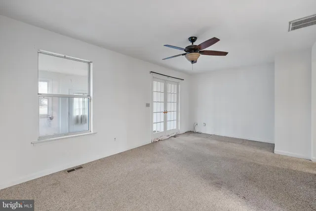 an empty room with chandelier fan and windows