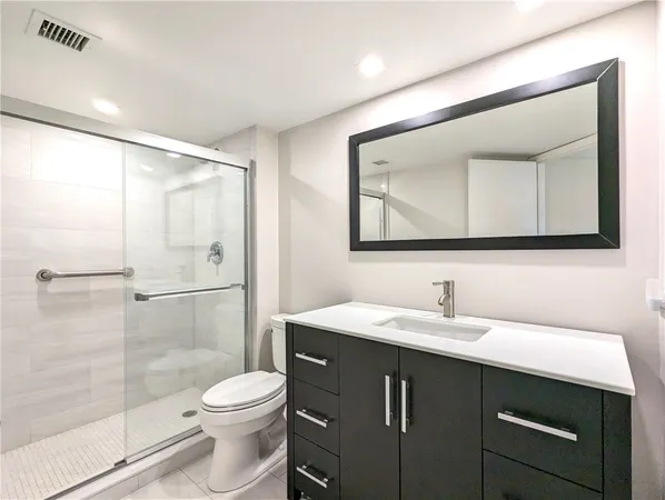 a bathroom with a toilet a sink a glass door a shower and a mirror