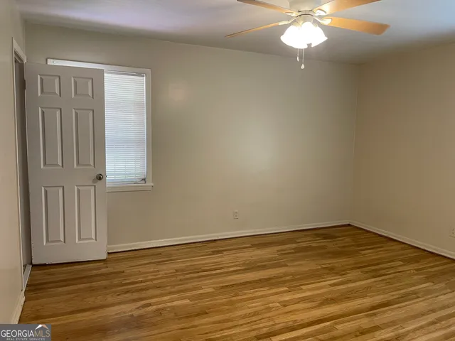 a view of an empty room with wooden floor and fan