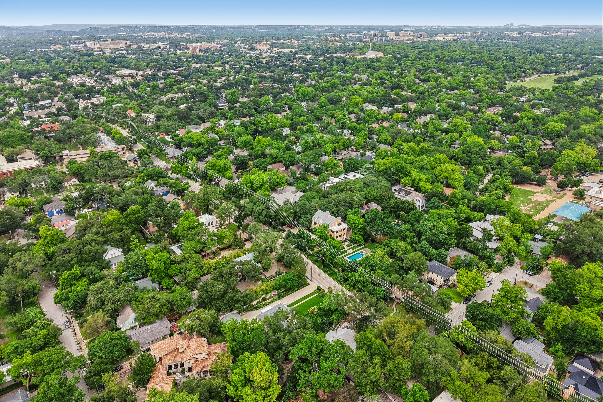 801 East 32nd Street Austin, TX 78705 - Photo 7 of 13 An aerial perspective reveals a tree-filled neighborhood with houses, some featuring private pools, and a distant city skyline.