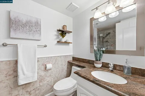 a bathroom with a granite countertop sink a toilet a mirror and shower
