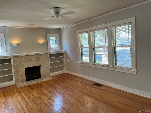 a view of an empty room with wooden floor fireplace and a window