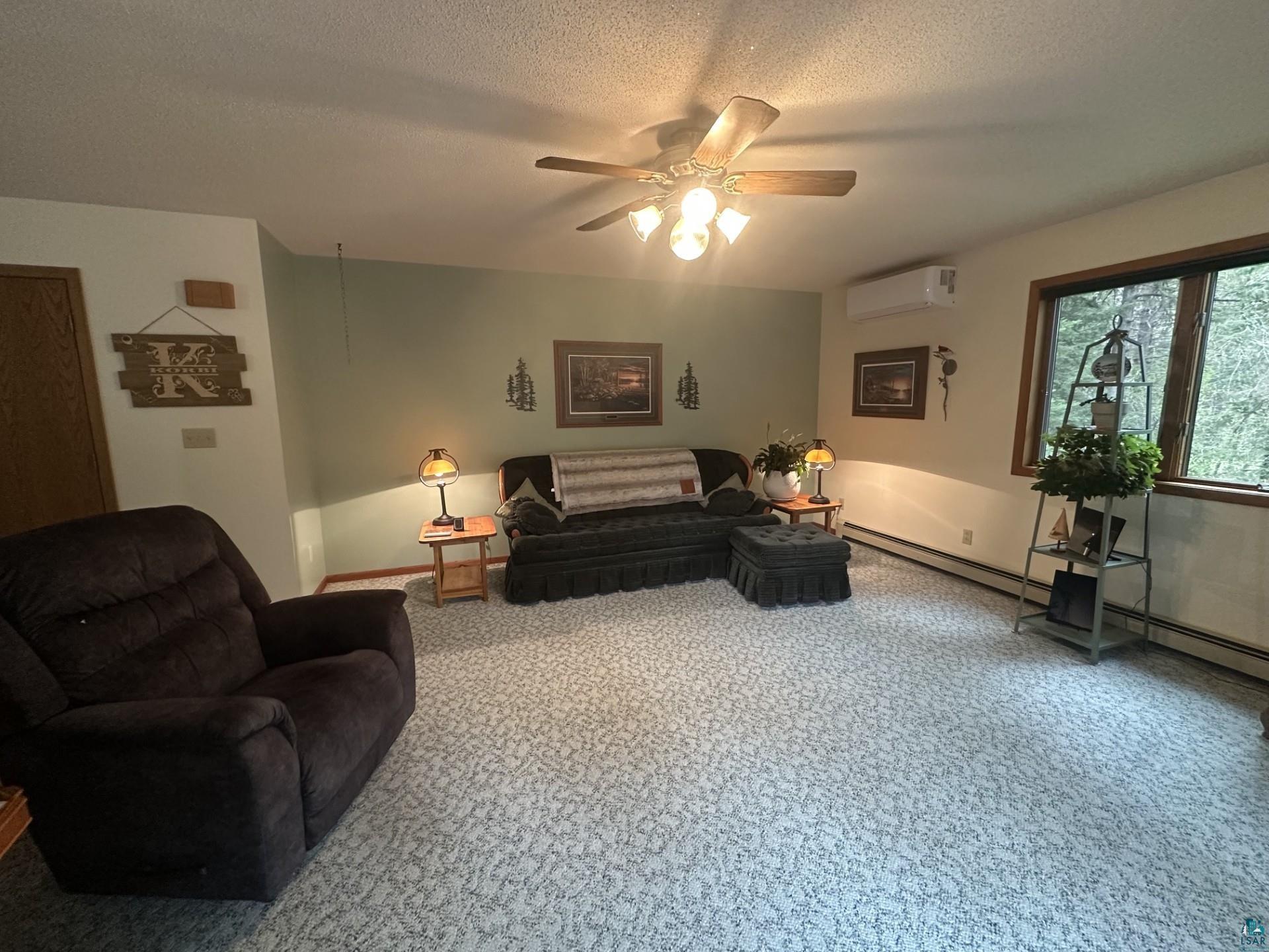 81 Hautaluoma Road Esko, MN 55733 - Photo 5 of 43 Spacious room featuring patterned carpeting, a wood-finish ceiling fan with integrated lighting, a ductless mini-split system, and a large window with natural light