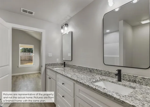 a bathroom with a granite countertop double vanity sink and a mirror