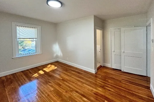 a view of an empty room with wooden floor and a window