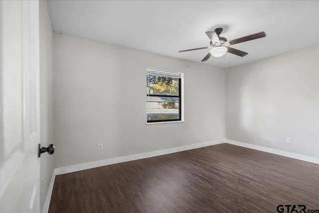 a view of an empty room with wooden floor and a ceiling fan