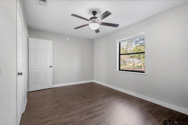 an empty room with wooden floor chandelier fan and windows