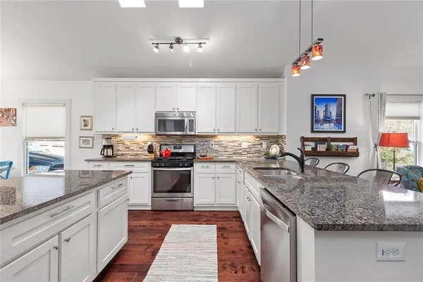 a kitchen with stainless steel appliances granite countertop a refrigerator a stove top oven a sink dishwasher and white cabinets with wooden floor