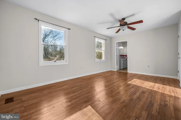 a view of an empty room with wooden floor and a kitchen