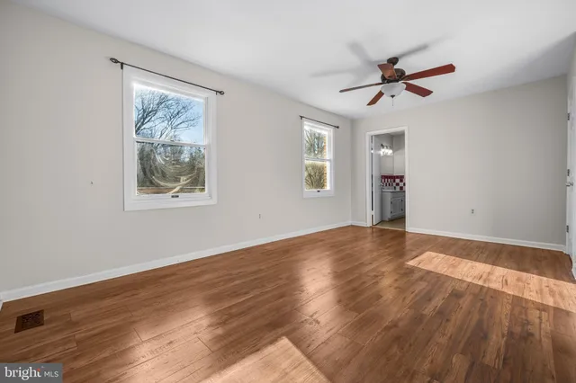 a view of an empty room with wooden floor and a kitchen