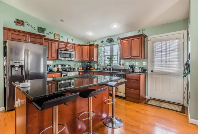 a kitchen with stainless steel appliances kitchen island granite countertop a refrigerator a stove a sink a dining table and chairs with wooden floor