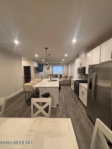 a kitchen with stainless steel appliances kitchen island granite countertop a sink a stove a refrigerator cabinets and a dining table with wooden floor