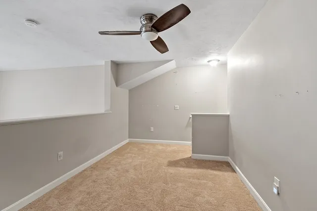 an empty room with a ceiling fan and kitchen view