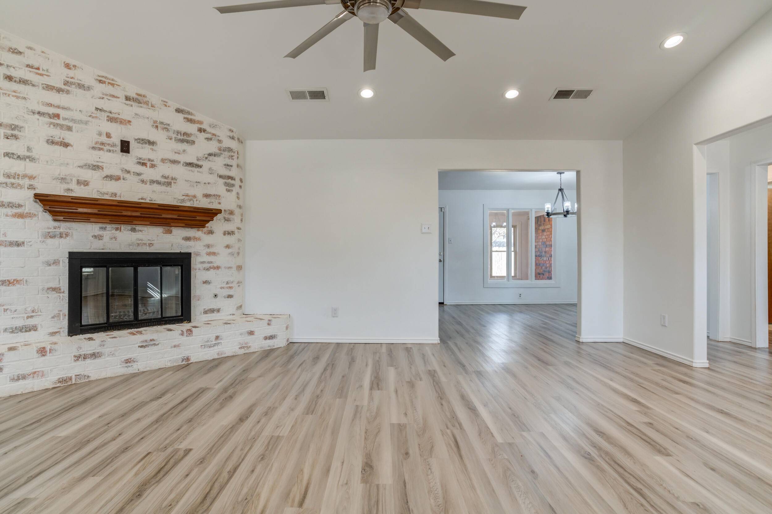 5504 73rd Street Lubbock, TX 79424 - Photo 9 of 39 an empty room with wooden floor a fireplace a ceiling fan and windows