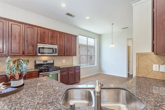 a kitchen with stainless steel appliances granite countertop a sink dishwasher stove and microwave with wooden floor