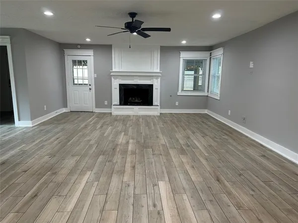 an empty room with wooden floor fireplace and windows