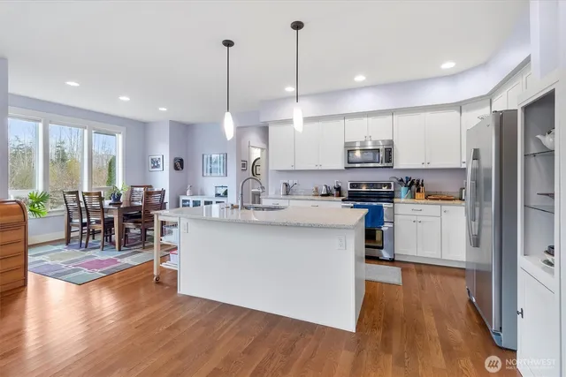 a kitchen with stainless steel appliances kitchen island granite countertop a stove a refrigerator a oven a sink with island and chairs with wooden floor