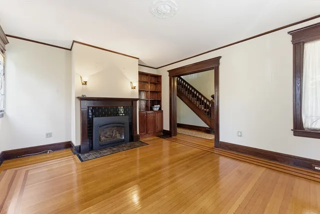 a view of an empty room with wooden floor fireplace and a window