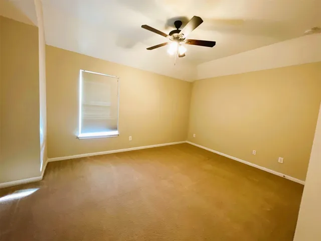 an empty room with a ceiling fan and carpet
