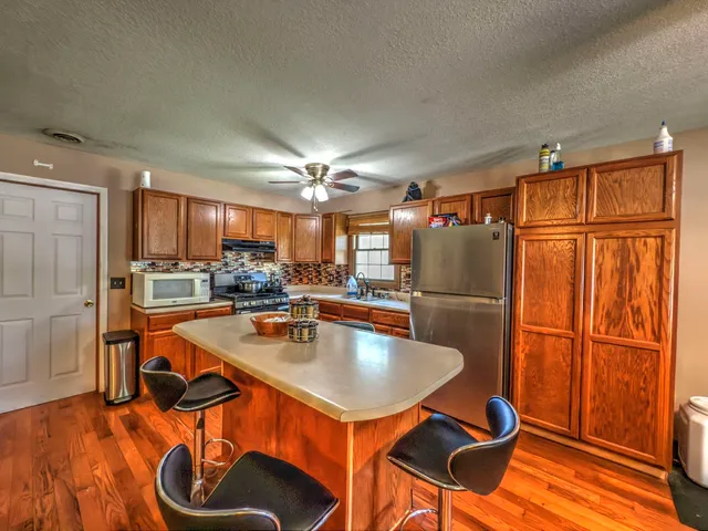 a kitchen with stainless steel appliances granite countertop a refrigerator a stove and a sink with wooden floor
