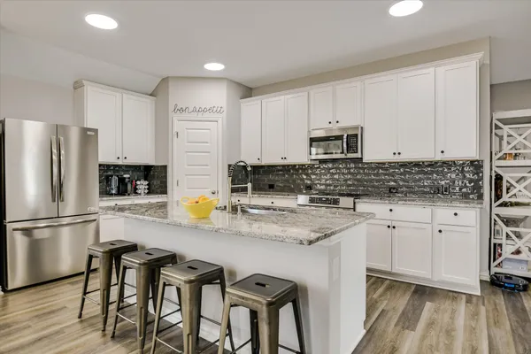 a kitchen with stainless steel appliances granite countertop a stove a sink dishwasher a refrigerator with white cabinets and wooden floor