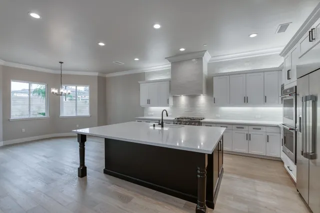 a large white kitchen with a refrigerator a sink dishwasher a stove and a dining table with wooden floor