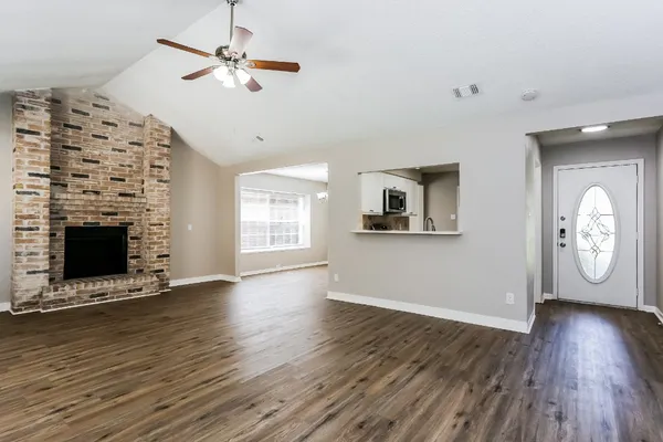 an empty room with wooden floor a ceiling fan a fireplace and windows