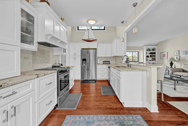 a large kitchen with stainless steel appliances a stove a sink dishwasher a refrigerator white cabinets and wooden floor