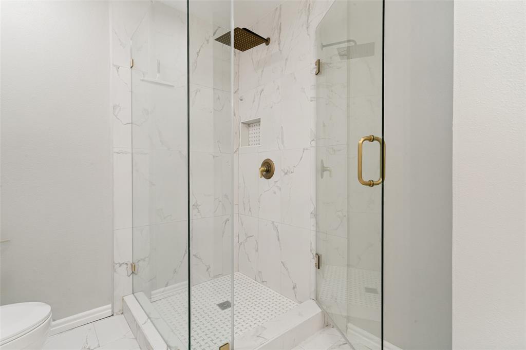 1712 East Peters Colony Road Carrollton, TX 75007 - Photo 22 of 25 Glass-enclosed shower featuring white marble-look tile walls, a built-in shower niche, and a gold-tone rain shower head