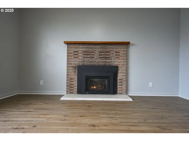 a view of an empty room with wooden floor and a fireplace