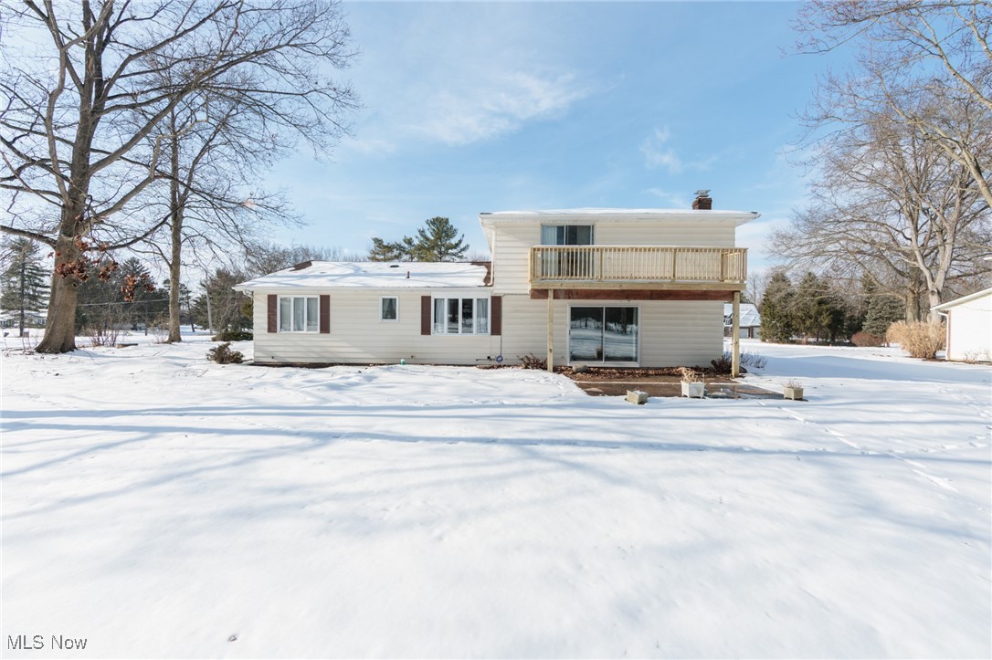 Snow covered rear of property featuring a wooden deck and a chimney