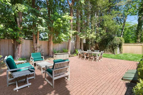 a view of a patio with a dining table and chairs with wooden fence and large trees