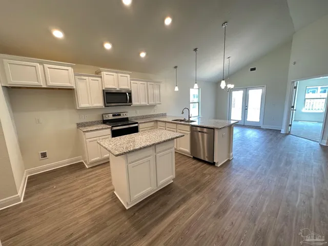 a kitchen with stainless steel appliances white cabinets a sink a stove a microwave and wooden floors