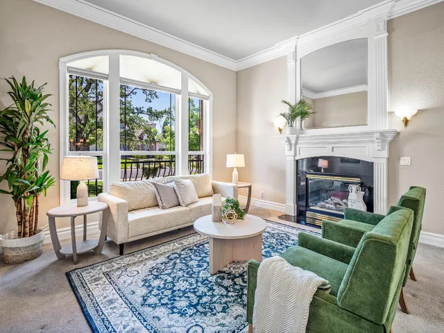 a living room with furniture a fireplace a table and a large window