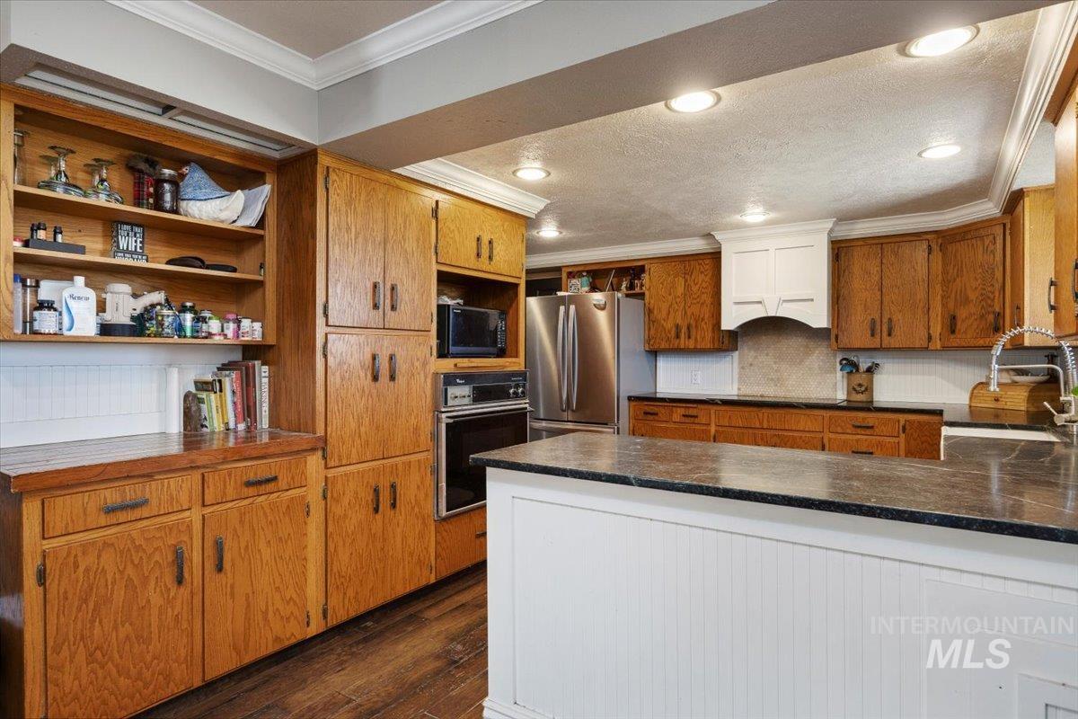 173 Main Line Ranch Road Rupert, ID 83350 - Photo 12 of 47 Kitchen featuring open shelves, crown molding, black appliances, dark wood-type flooring, and brown cabinets