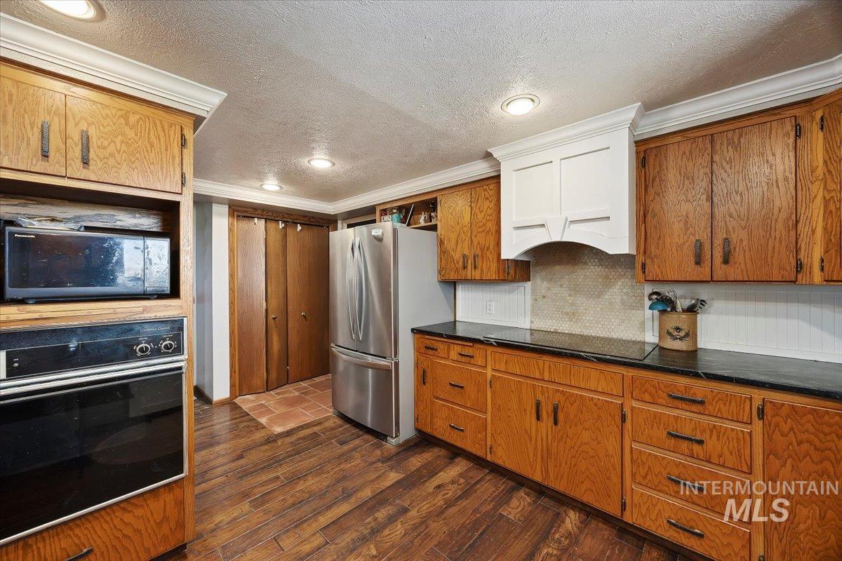173 Main Line Ranch Road Rupert, ID 83350 - Photo 14 of 47 Kitchen featuring black appliances, dark wood finished floors, a textured ceiling, crown molding, and tasteful backsplash