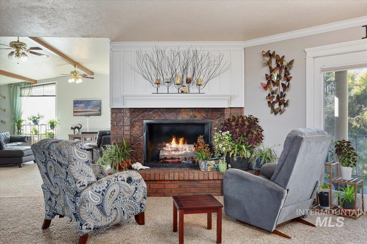 173 Main Line Ranch Road Rupert, ID 83350 - Photo 6 of 47 Living area featuring a textured ceiling, a brick fireplace, carpet floors, beamed ceiling, and ceiling fan