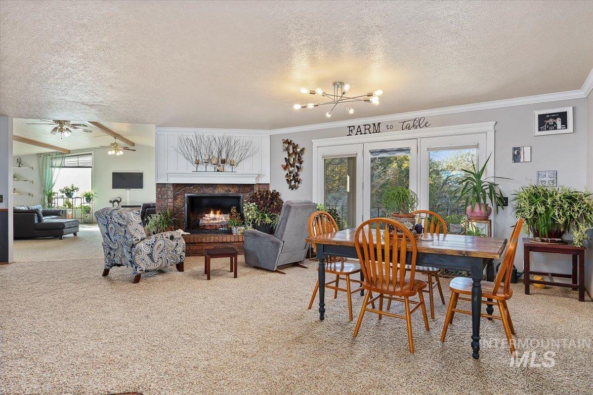 173 Main Line Ranch Road Rupert, ID 83350 - Photo 8 of 47 Dining area with light carpet, a warm lit fireplace, a textured ceiling, beam ceiling, and a chandelier