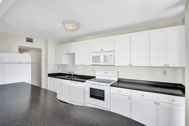 a kitchen with granite countertop a stove a sink and white cabinets
