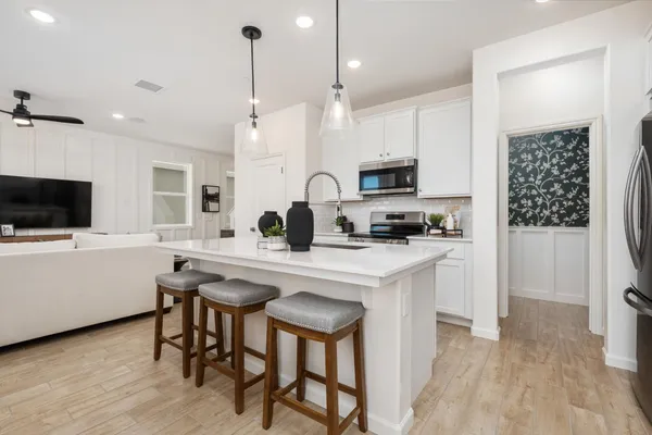 a kitchen with stainless steel appliances a stove a sink a refrigerator a microwave a sink and white cabinets with wooden floor