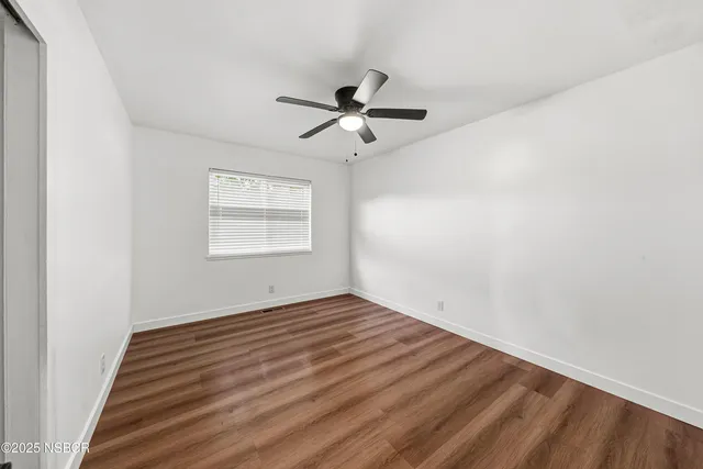 an empty room with wooden floor ceiling fan and windows