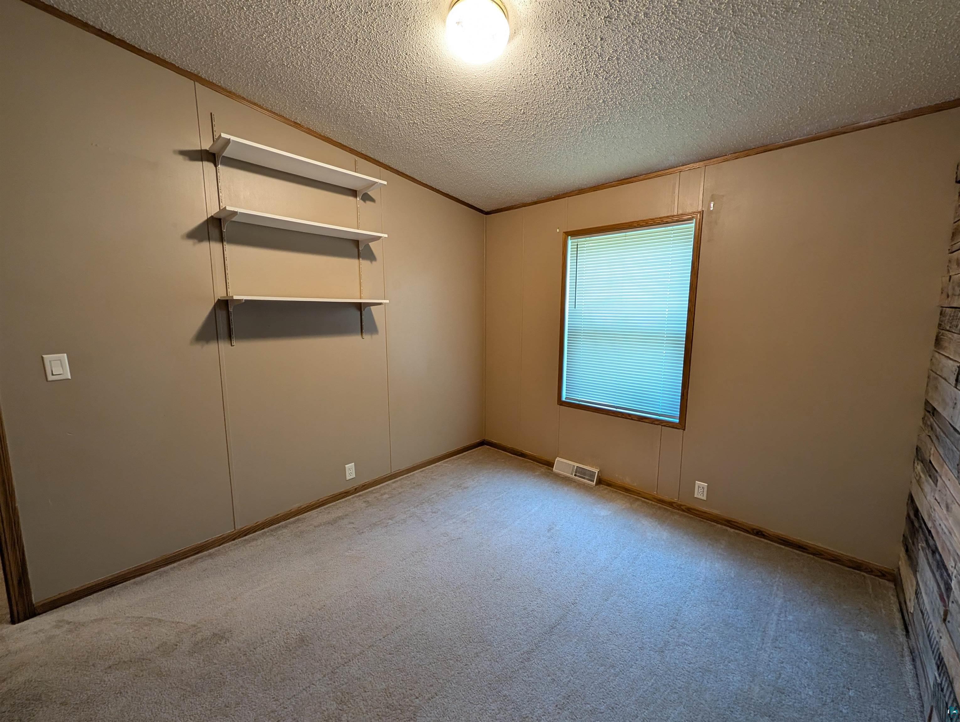 3945 Maple Street Kettle River, MN 55757 - Photo 20 of 41 Carpeted room featuring a single window with blinds, wall paneling, and three wall-mounted shelves