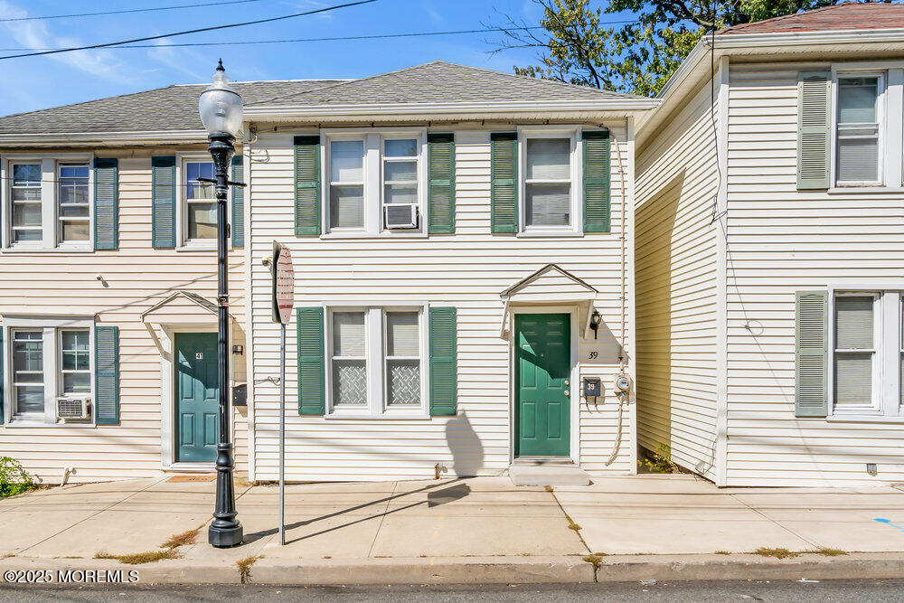 a view of a brick house with small yard plants and large tree